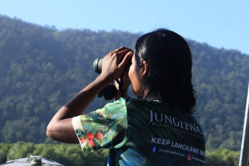 A person wearing a shirt with 'JUNGLE' and 'KEEP LANGKAWI WILD' text, holding binoculars. 5