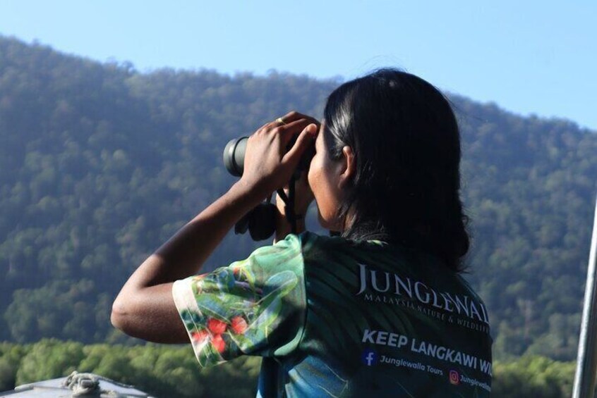 A person wearing a green shirt with 'JUNGLE' and 'KEEP LANGKAWI WILD' text, taking a photo with a camera. 4