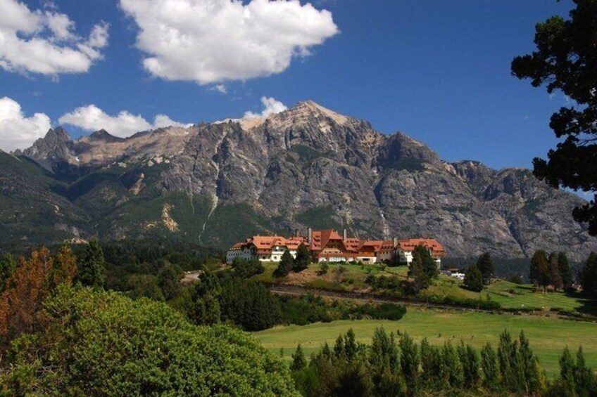 A mountain lodge with a red roof, surrounded by lush greenery and a backdrop of rugged mountains. 4