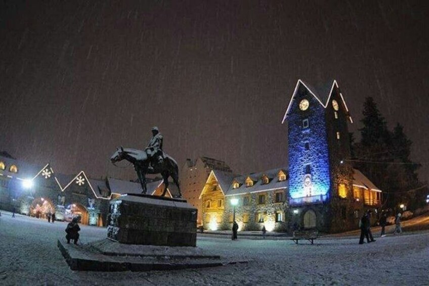 A statue on a pedestal, a snow-covered square, and a building with a clock tower. 5