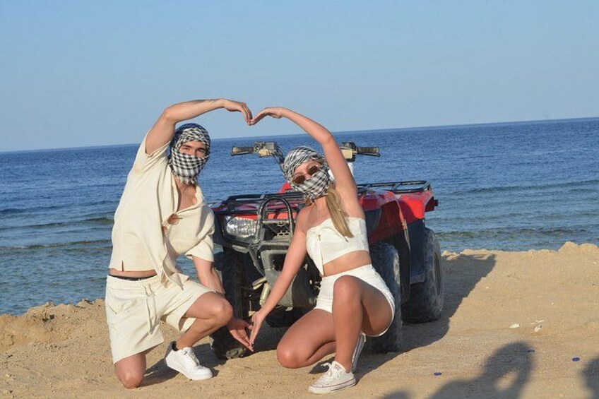 Two people making a heart shape with their hands, a red ATV, and a beach with the sea in the background. 3