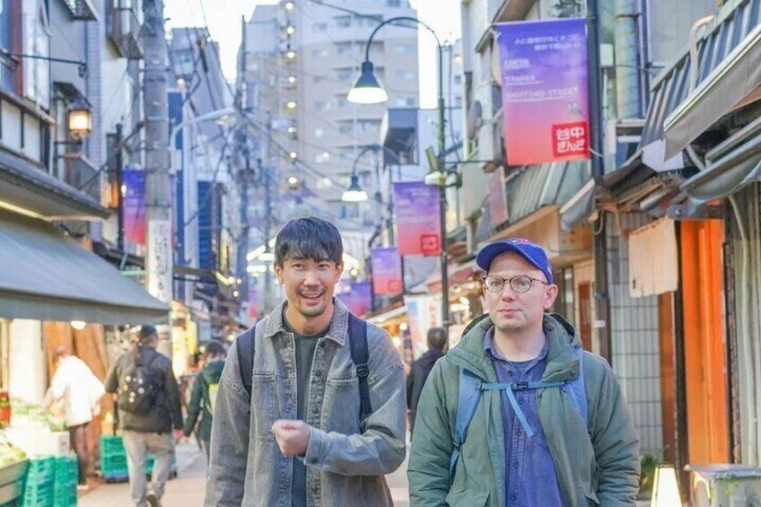 Two people walking on a busy street with shops and buildings. 1