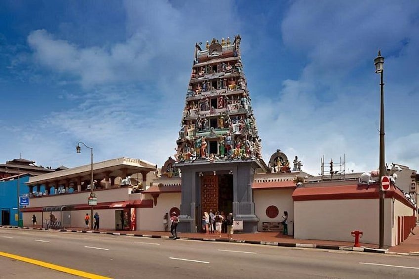 A multi-tiered temple with intricate carvings and statues, a street in the foreground, and a clear blue sky. 3