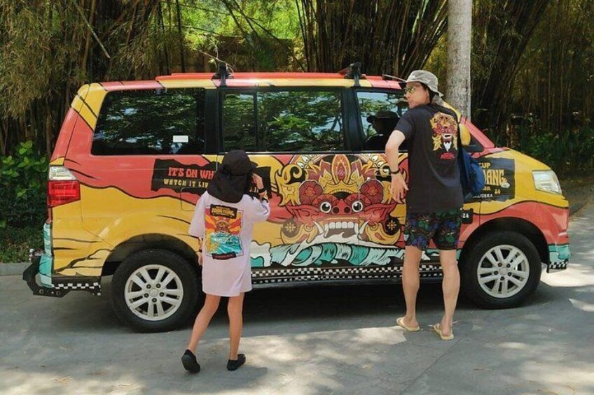 A colorful bus with a vibrant mural, parked on a paved road with trees in the background. 2