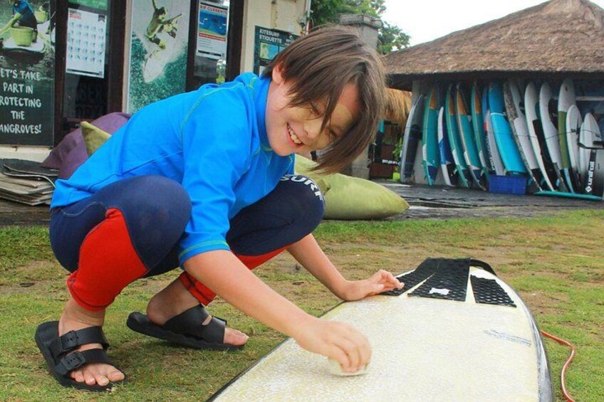 A person crouching on grass, working on a surfboard. 3