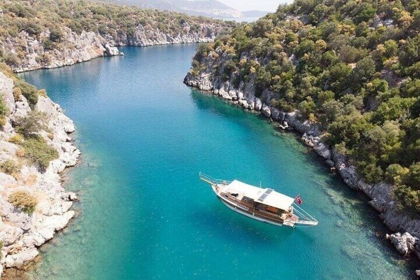 A boat on a turquoise sea surrounded by rocky cliffs and dense greenery. 2