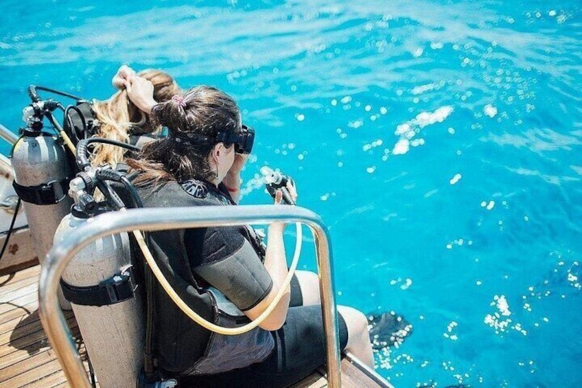 A person in a diving suit preparing to enter the water, with a diving tank and regulator visible. 4