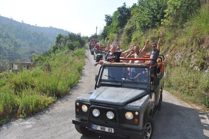 A convoy of off-road vehicles on a narrow road surrounded by greenery. 5