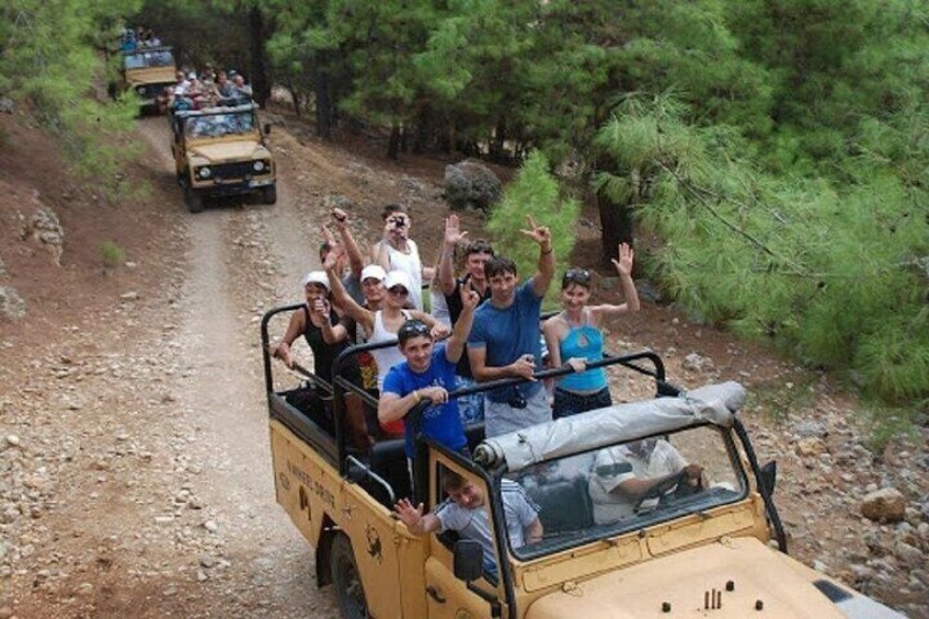 A group of people on a safari vehicle driving on a dirt road surrounded by trees. 3