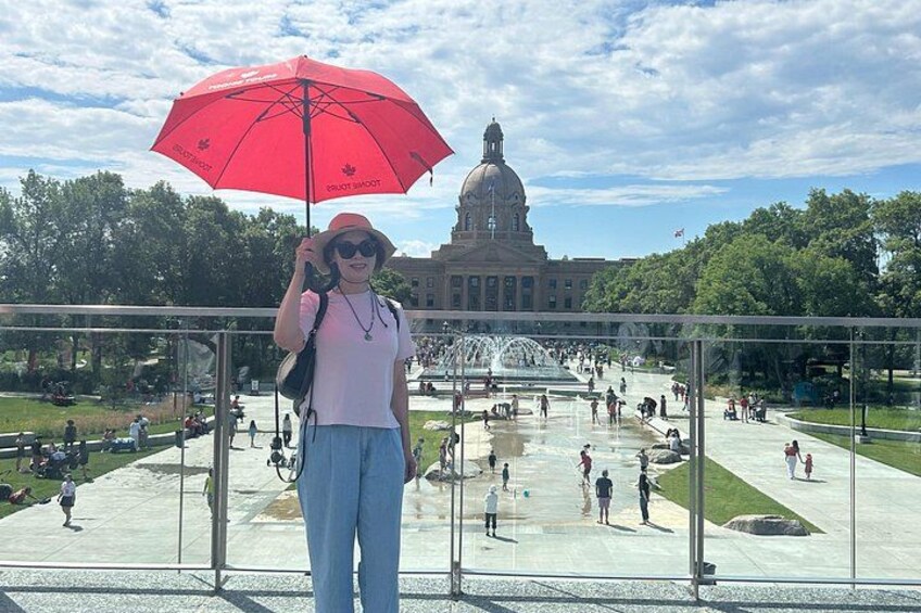A person standing on a bridge with a red umbrella, overlooking a large fountain and a building with a dome in the background. 5
