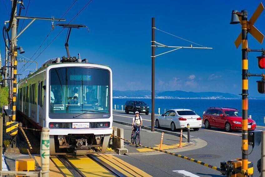 A tram at a railway crossing with cars and a cyclist nearby. 3