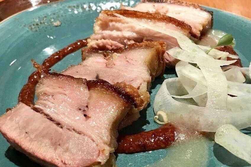 Sliced roasted pork with a crispy skin, accompanied by shredded cabbage and a dark sauce. 2