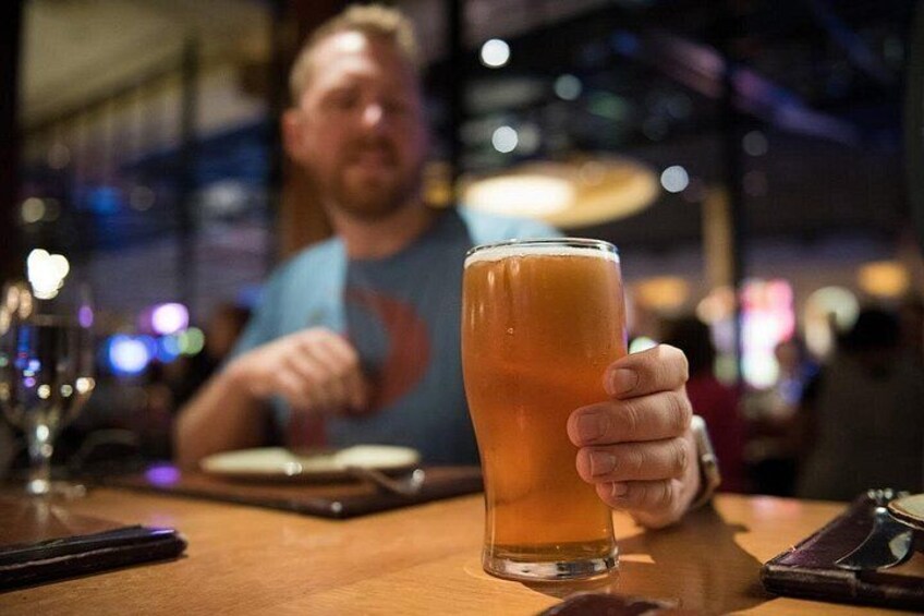 A person holding a tall glass of amber liquid, likely beer, at a bar with a blurred background. 4