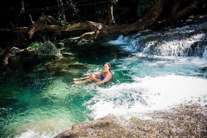 A person floating in a clear, turquoise pool with a waterfall in the background. 4