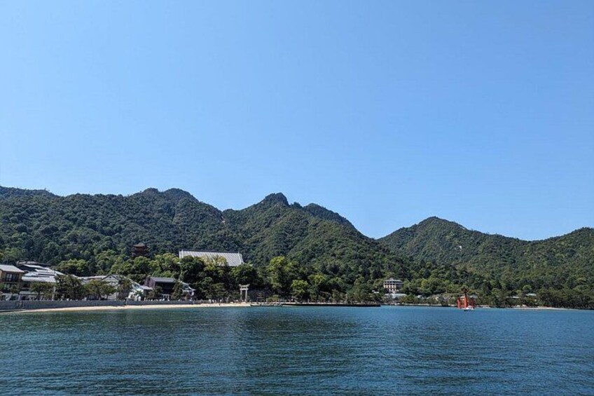 A coastal town with buildings, a clear sky, and green hills in the background. 2