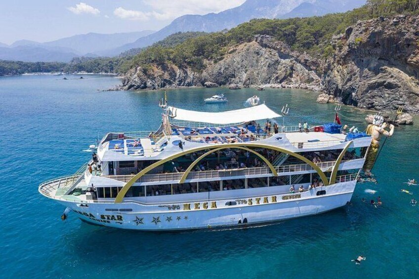 A large white cruise ship with a curved golden railing, surrounded by clear blue water and rocky cliffs. 1