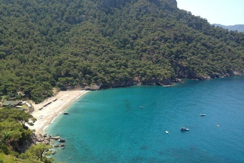 A coastal landscape with a beach, clear turquoise waters, and a forested hill. 3
