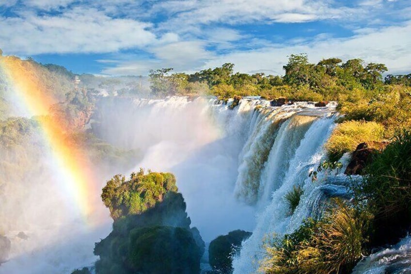 A waterfall with a rainbow, lush greenery, and rocky outcrops. 4