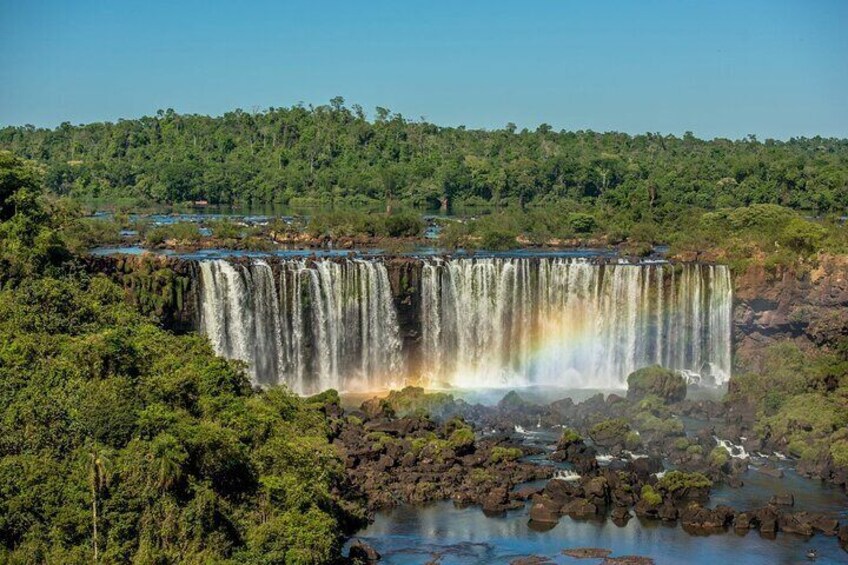 A large waterfall with a rainbow, surrounded by dense forest and rocky terrain. 5
