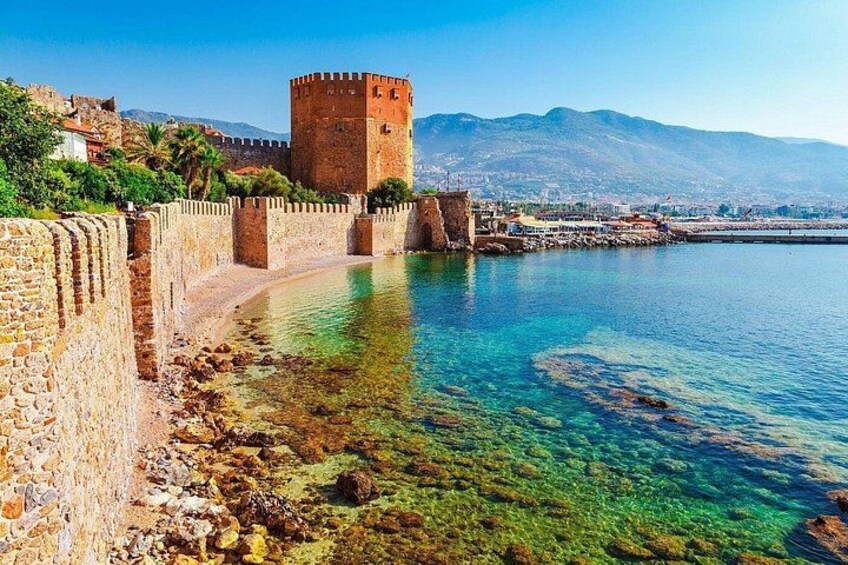 A coastal city with a historic stone wall, a tower, and clear blue waters. 2
