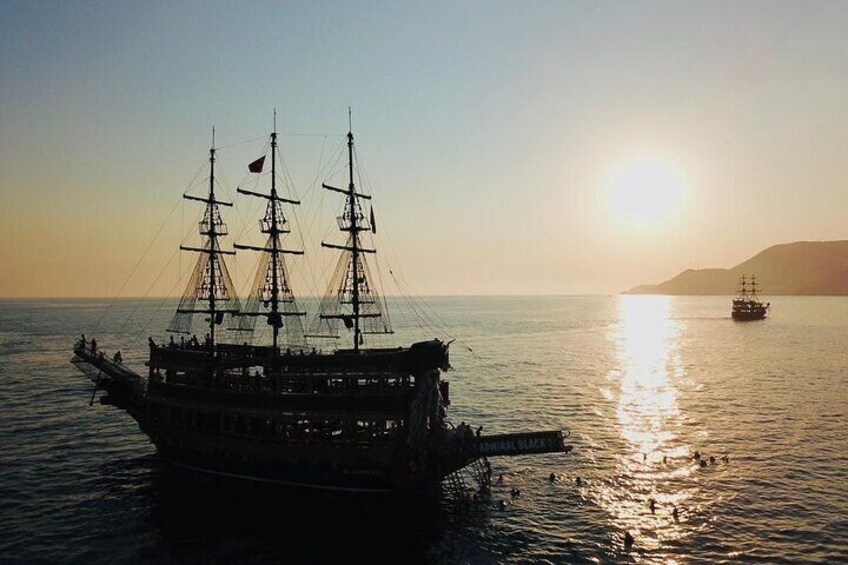 A large sailing ship with multiple masts and a flag, anchored in calm waters during sunset. 5