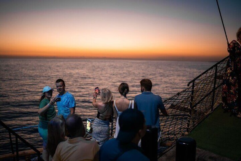 A group of people on a boat deck during sunset, with the ocean in the background. 4