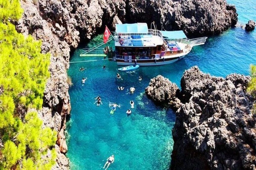 A boat with people swimming in clear blue water near rocky cliffs. 1