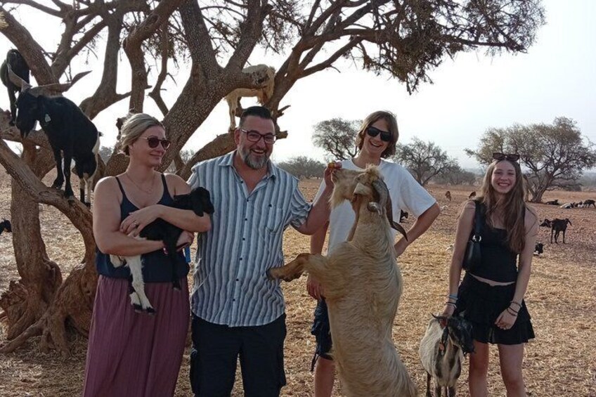 A group of people with a camel and goats in a dry, open landscape with sparse trees. 5