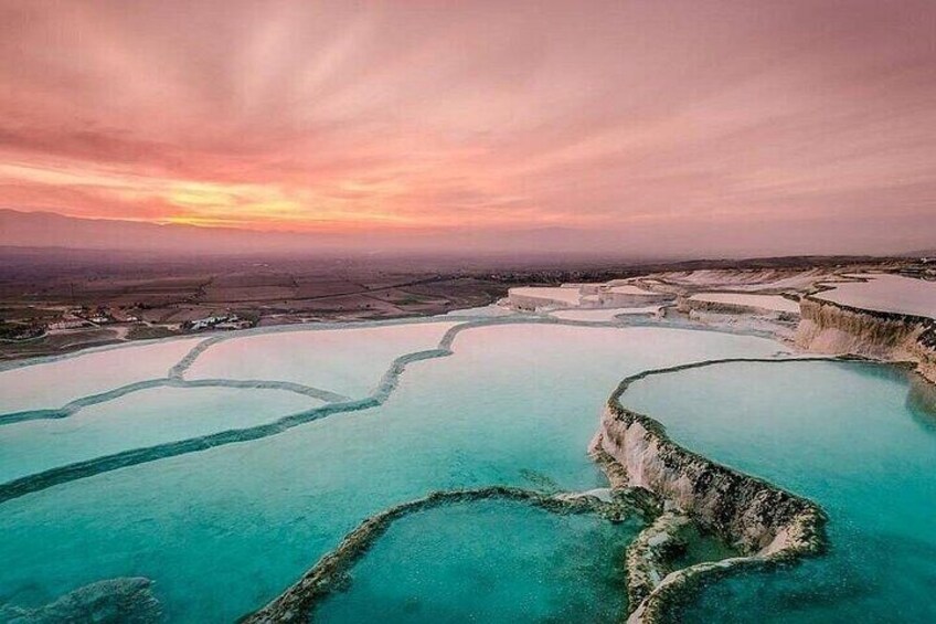 Terraced pools with clear turquoise water, a sunset sky, and distant land. 1