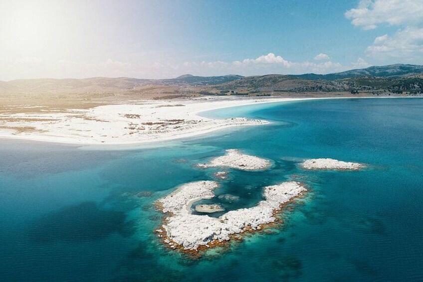 A coastal landscape with a sandy beach, clear turquoise waters, and a distant mountain range. 3
