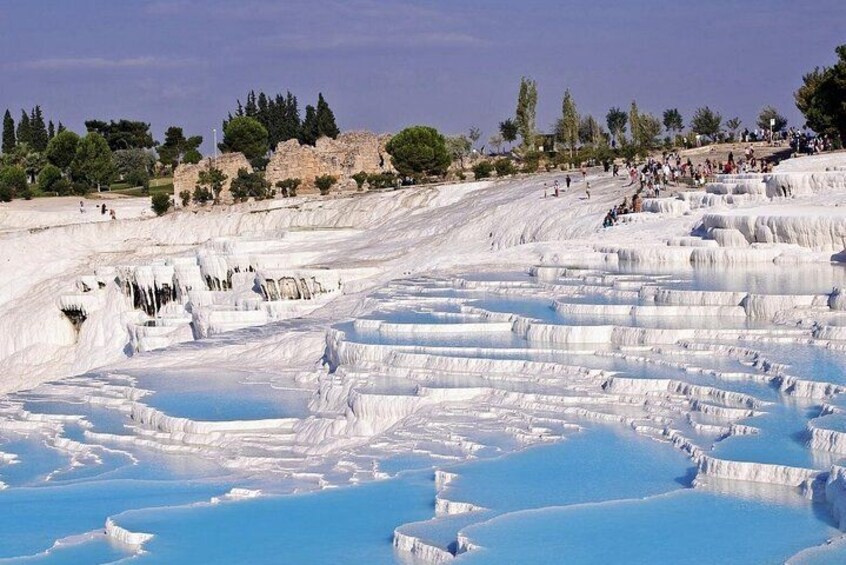 Terraced travertine formations with clear blue pools, surrounded by trees and a hilly landscape. 5