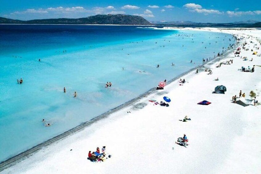 A beach with clear turquoise water, white sand, and people sunbathing and swimming. 4