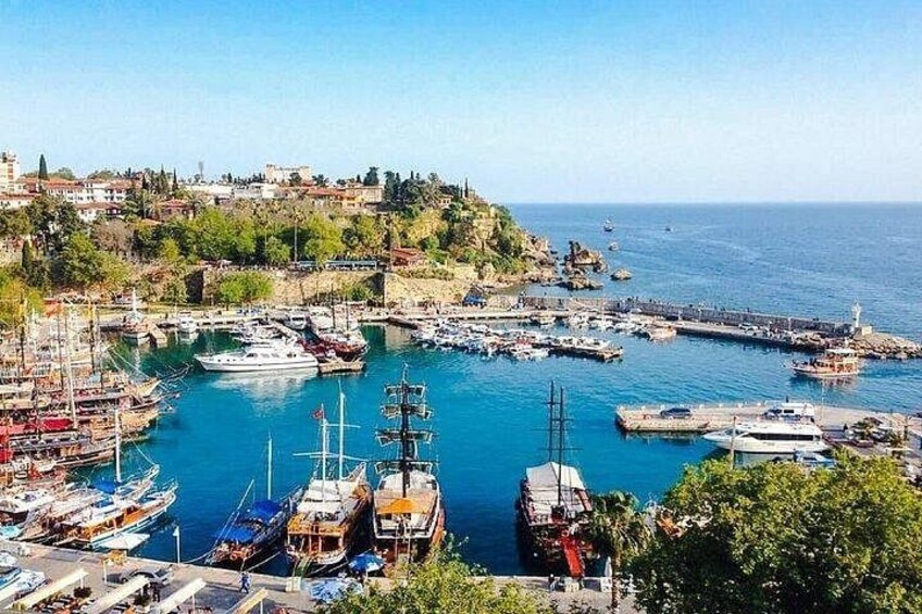 A coastal marina with boats, a lighthouse, and a hilly town in the background. 1