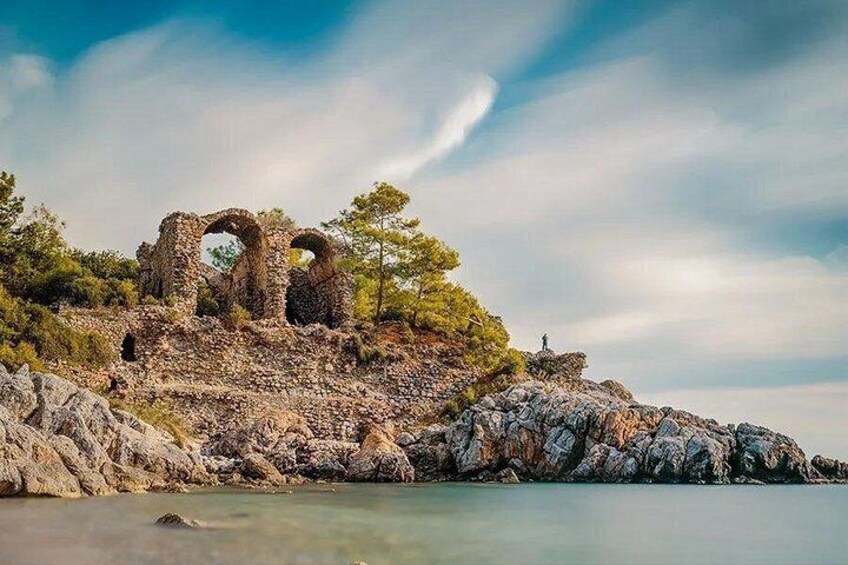 Ancient ruins on a rocky hillside with a calm sea in the foreground. 5