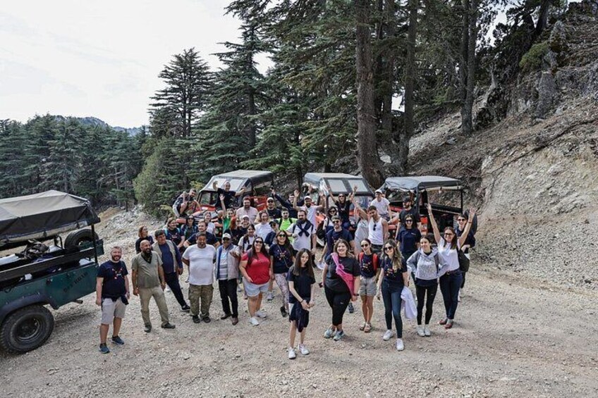 A group of people gathered around a vehicle on a gravel path in a forested area. 4