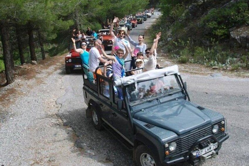 A group of people on a safari vehicle driving on a road surrounded by trees. 3