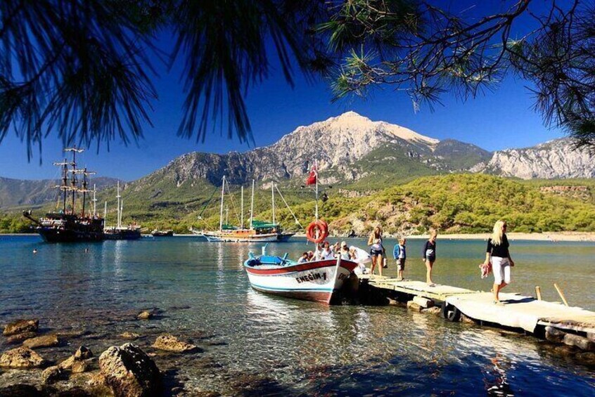 A boat docked at a pier with people on it, a large ship in the background, and mountains in the distance. 4