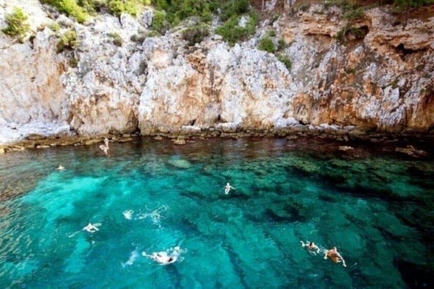 A clear blue sea with swimmers, rocky cliffs, and sparse vegetation. 5
