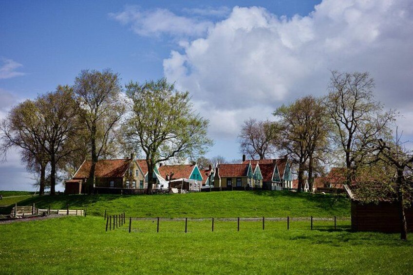 A rural landscape with a row of traditional houses on a grassy hill, a fence in the foreground, and a clear sky. 5