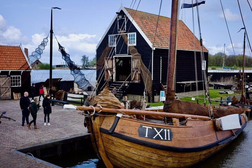 A wooden boat named TX11 docked at a pier, with a building and people in the background. 3