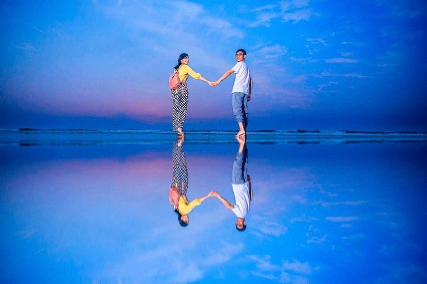 Two people holding hands on a reflective surface with a blue sky and horizon in the background. 5