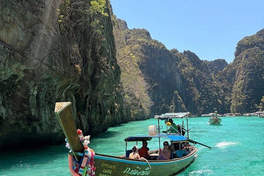 A boat with passengers, clear turquoise water, and rocky cliffs in the background. 1