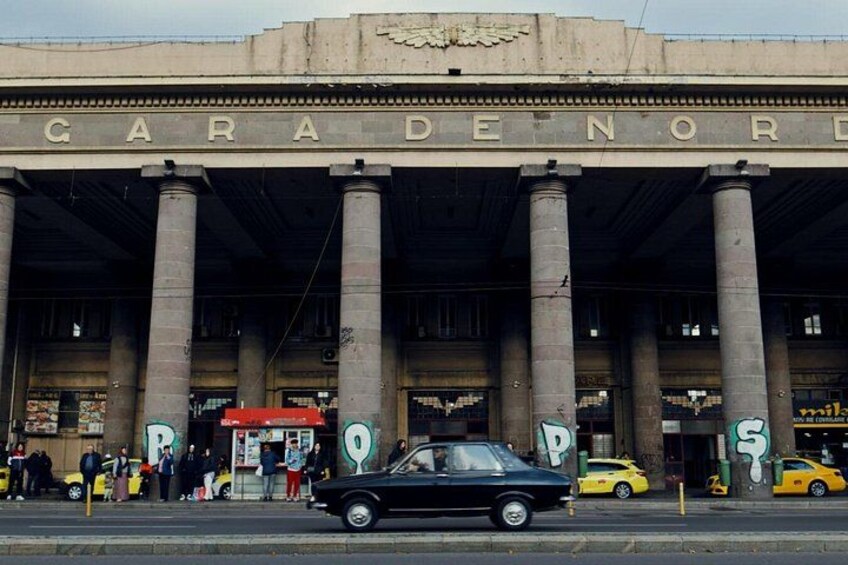 A building with columns and the sign 'GARADENORD' above. There are cars parked in front and people standing around. 3