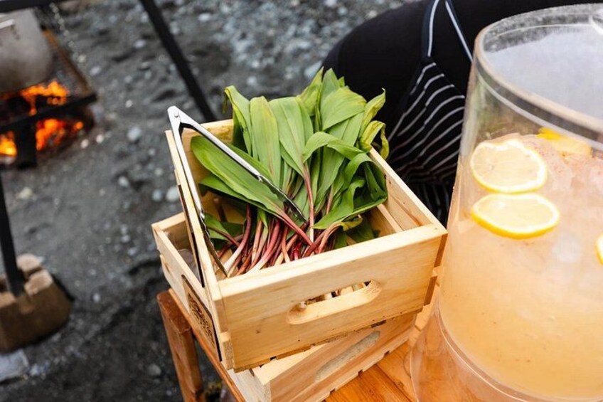 A wooden crate with green leaves, a glass of iced drink with lemon slices, and a grill with flames. 3