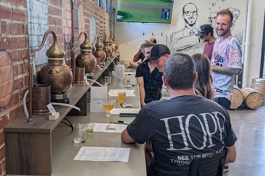 A bar with copper stills, a counter with glasses and menus, and a mural on the wall. 3