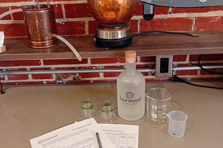 A countertop with a bottle of burwood, three small green glasses, a clear measuring cup, and a document titled 'On-Marking Guide'. 1