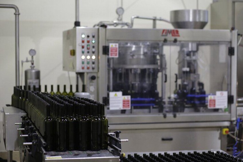 A machine with bottles in a production line, surrounded by control panels and safety signs. 4