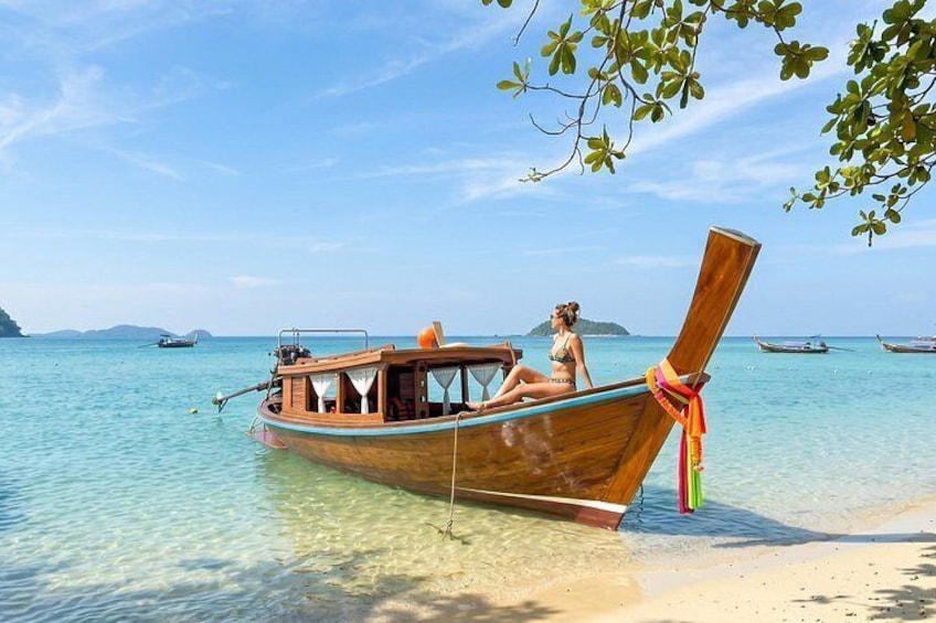 A wooden boat with a woman on it, anchored near a beach with clear water and distant islands. 5