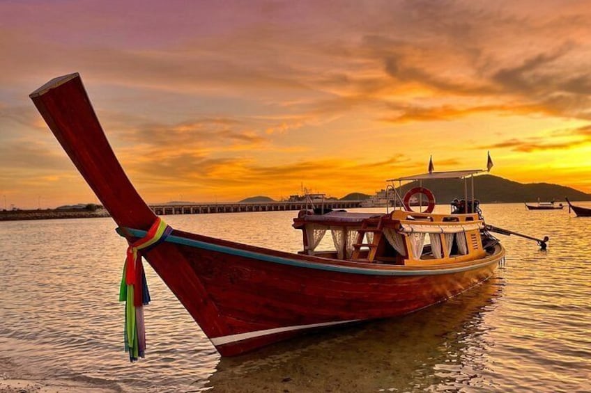 A traditional wooden boat with a long tail, docked at a pier during sunset. 2