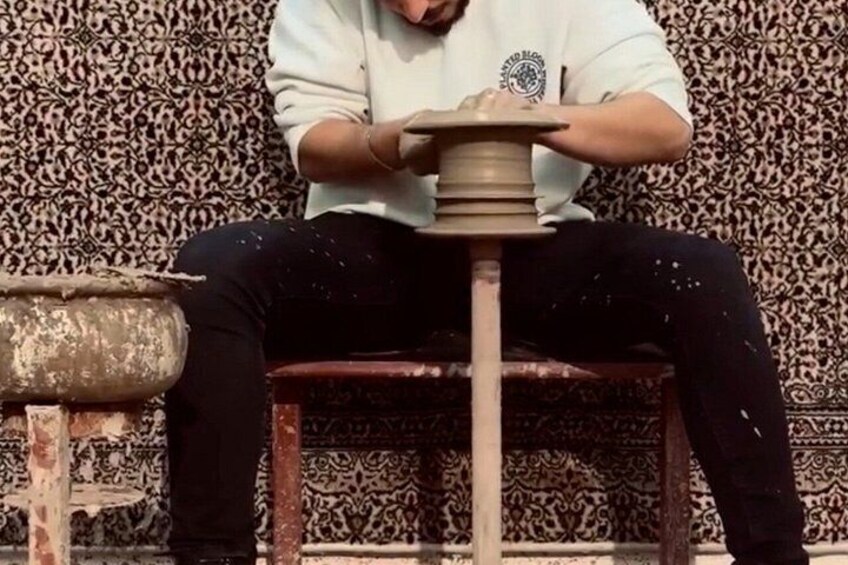 A person sitting on a stool, holding a pottery wheel. 1